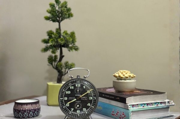 Books, candle, small plant, and alarm clock on a table representing preparation for Friday Sunnahs